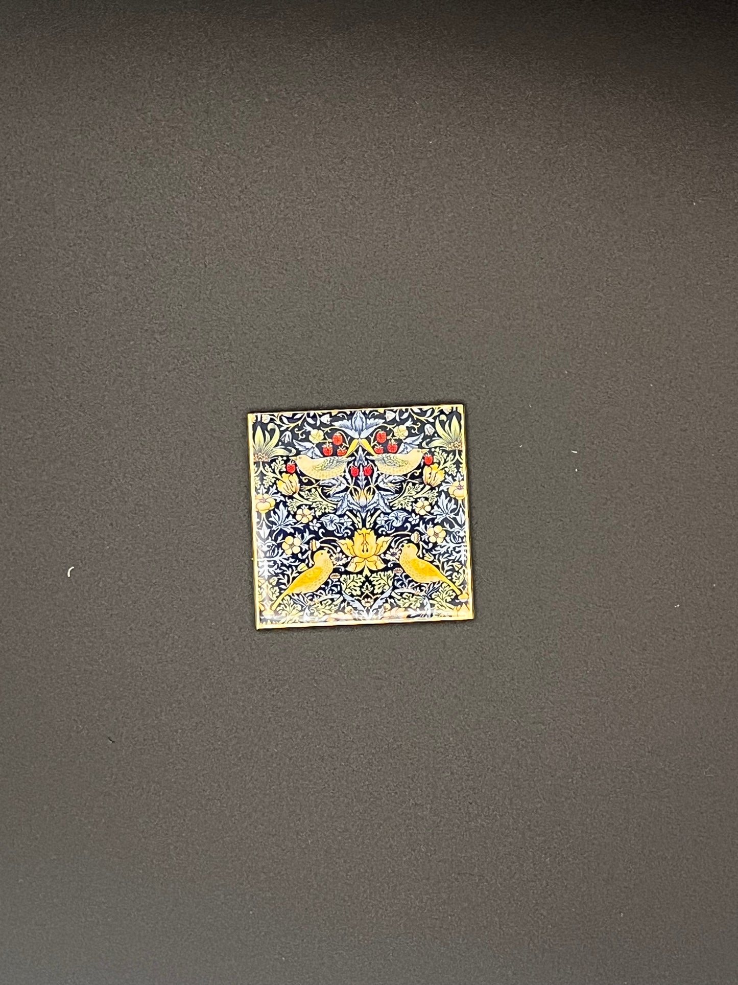 Small decorative tile needle minder with floral pattern on a dark gray background