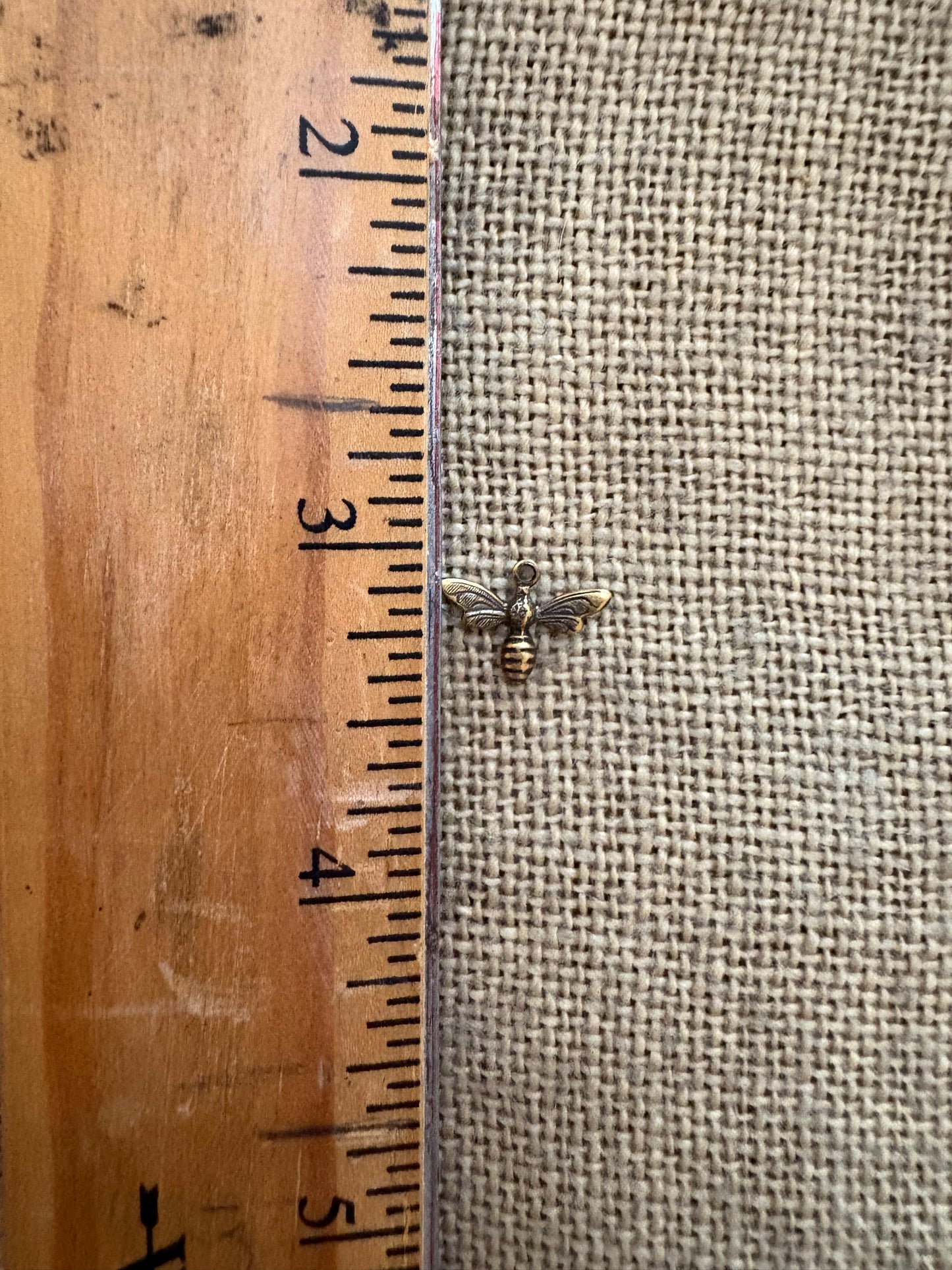 Small bee-shaped charm next to a wooden ruler for scale