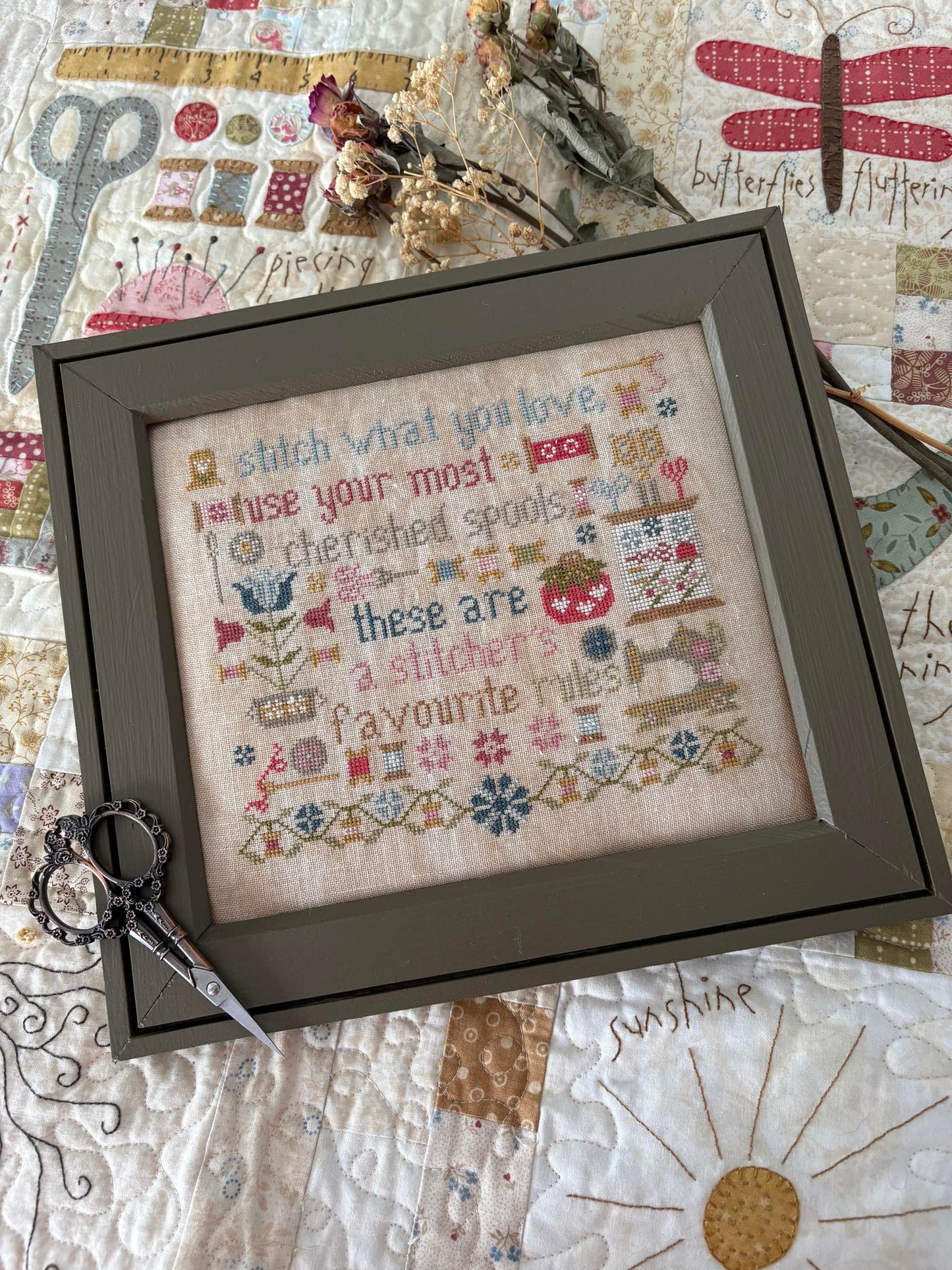 Framed cross-stitched sampler with decorative elements on a quilted background