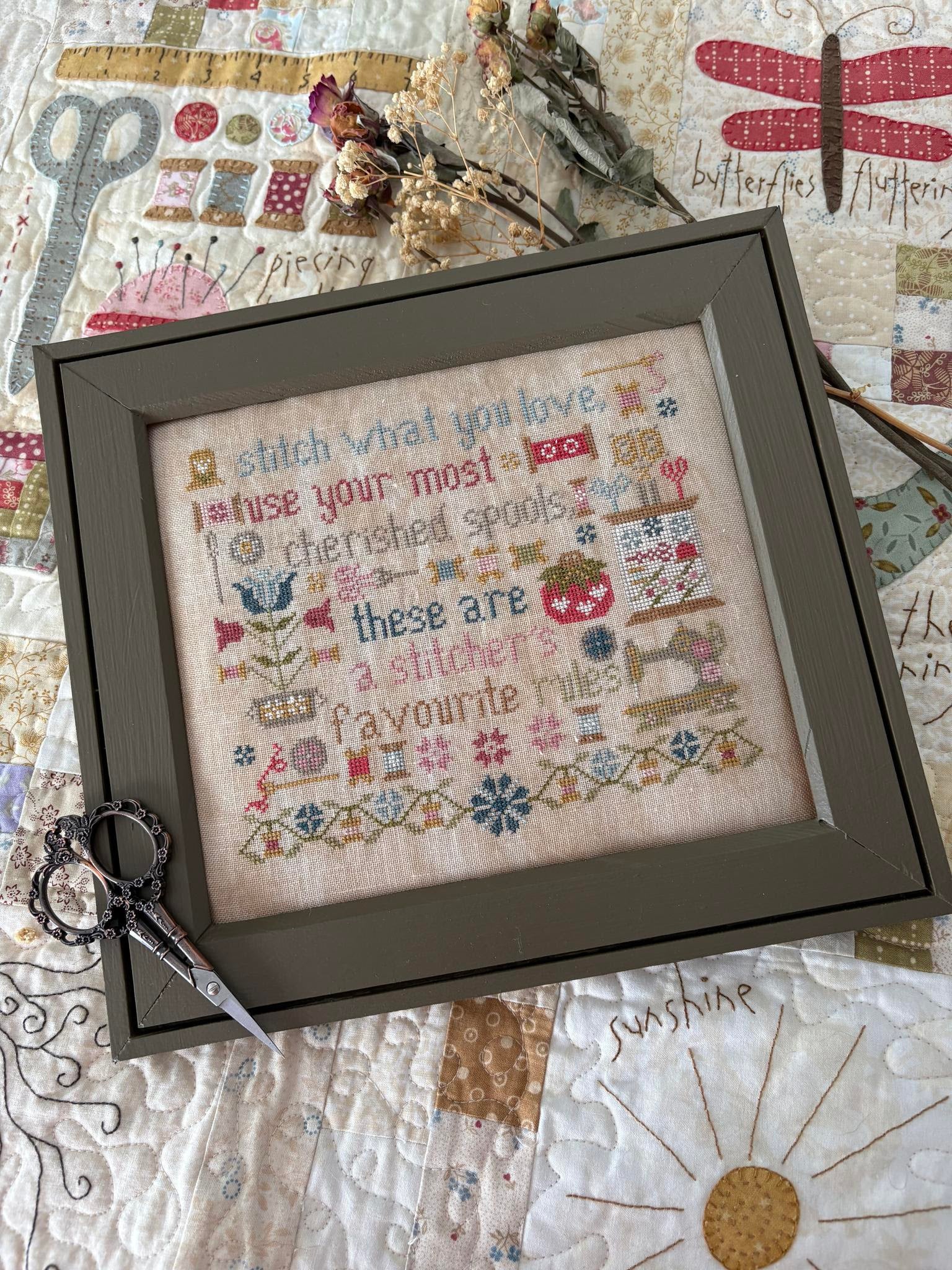 Framed cross-stitched sampler with decorative elements on a quilted background