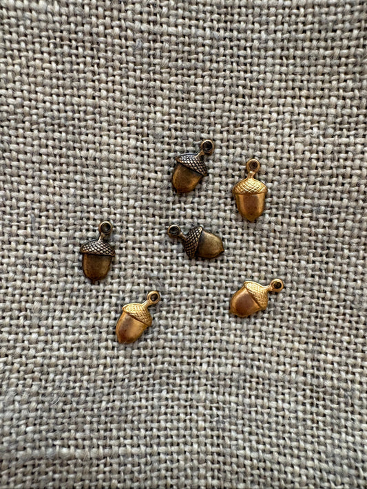 Small bronze acorn-shaped charm on a textured fabric background