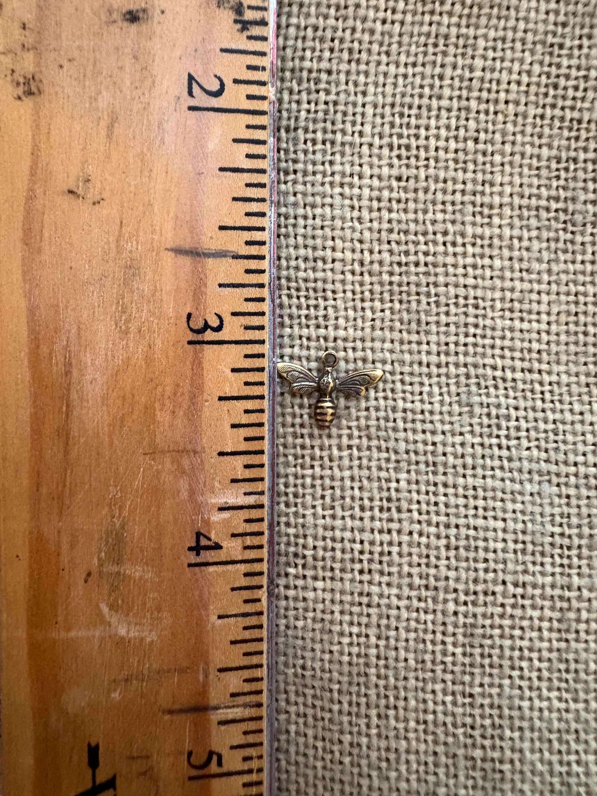 Small bee-shaped charm next to a wooden ruler for scale