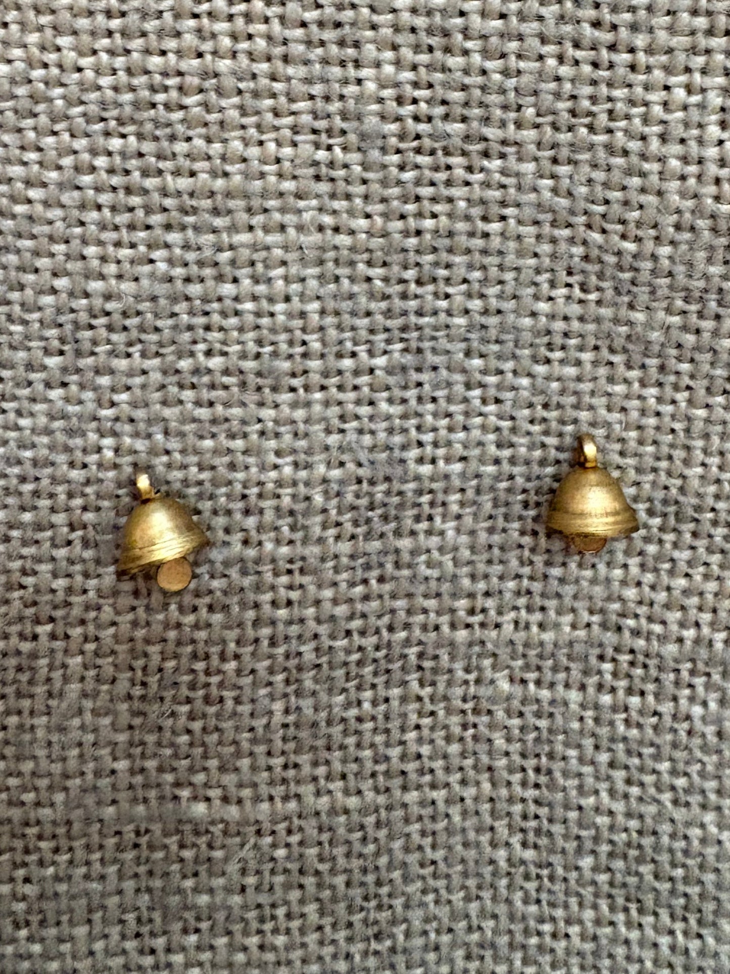 Two small brass bells on a gray fabric background
