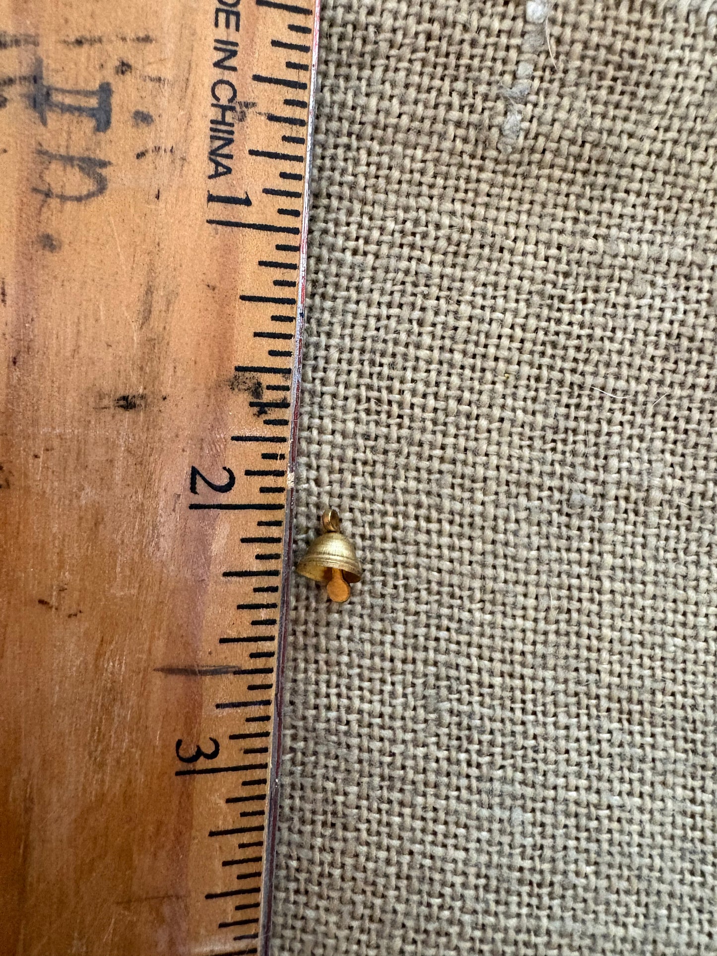 Small gold object next to a ruler on a textured fabric background