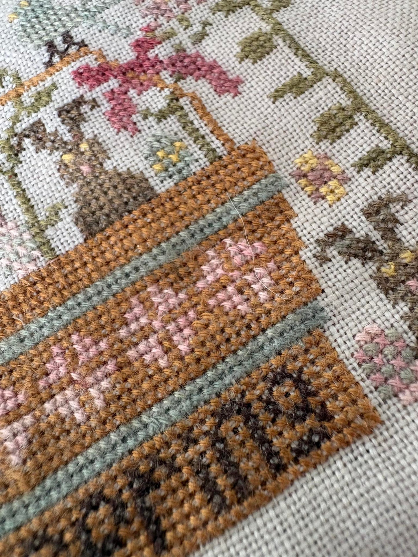 Close-up of a cross-stitched design featuring a basket with flowers and leaves.