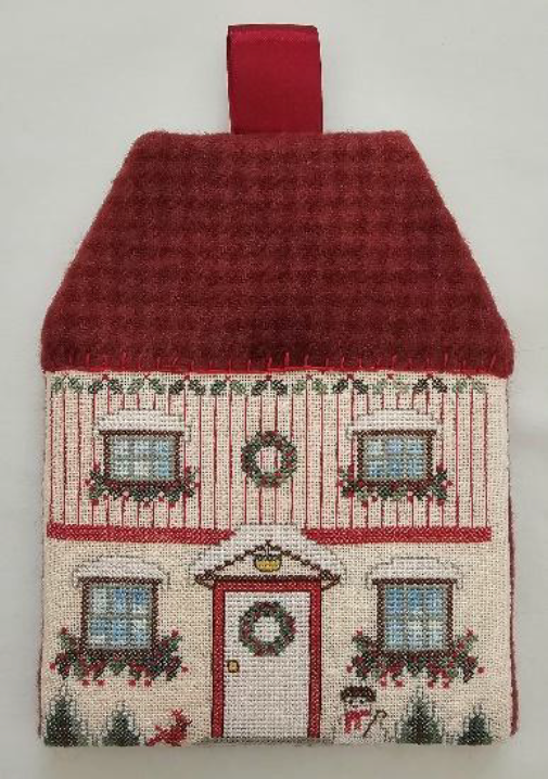 Decorative house-shaped pillow with a red roof and festive decorations on a plain background