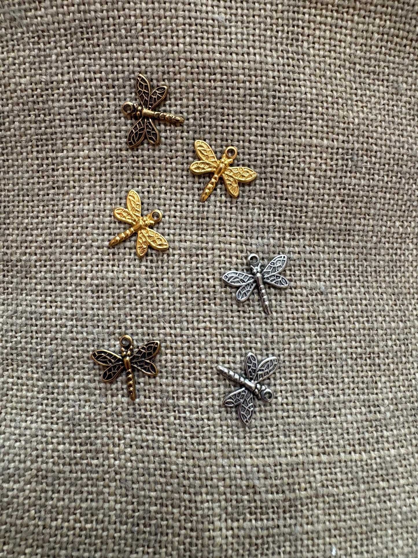 Set of dragonfly-shaped charms in 3 colors on a textured fabric background
