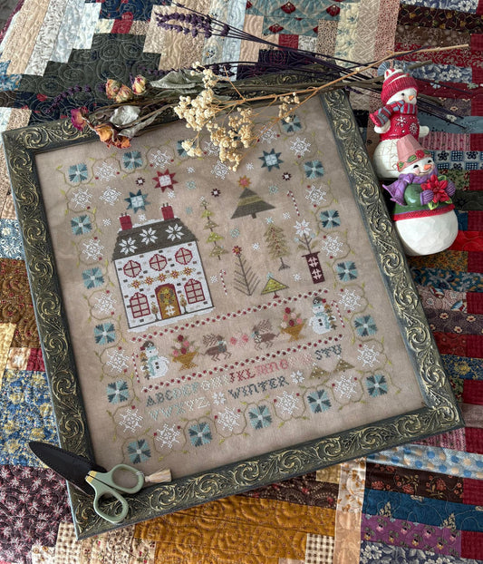 Decorative cross-stitch piece with a house design on a quilted surface.