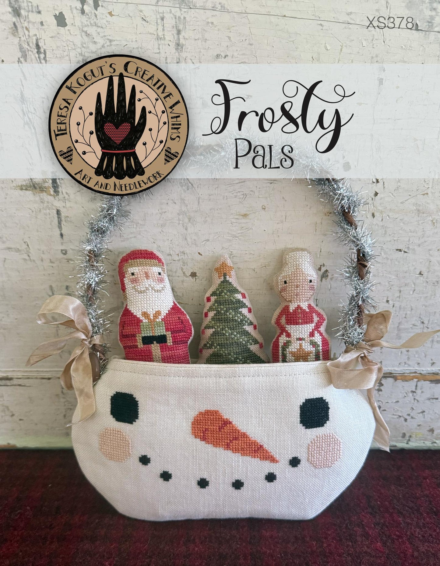 Decorative basket with knitted figures of Santa Claus, a tree, and a child, labeled 'Frosty Pals', on a rustic background.
