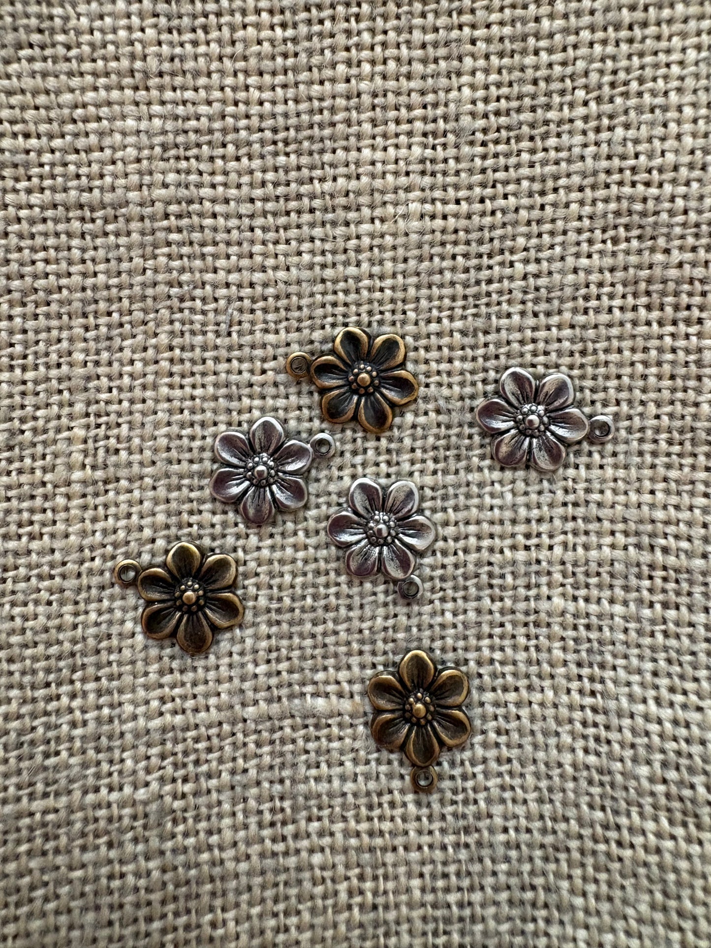 Bronze flower-shaped metal charms on a textured beige fabric background