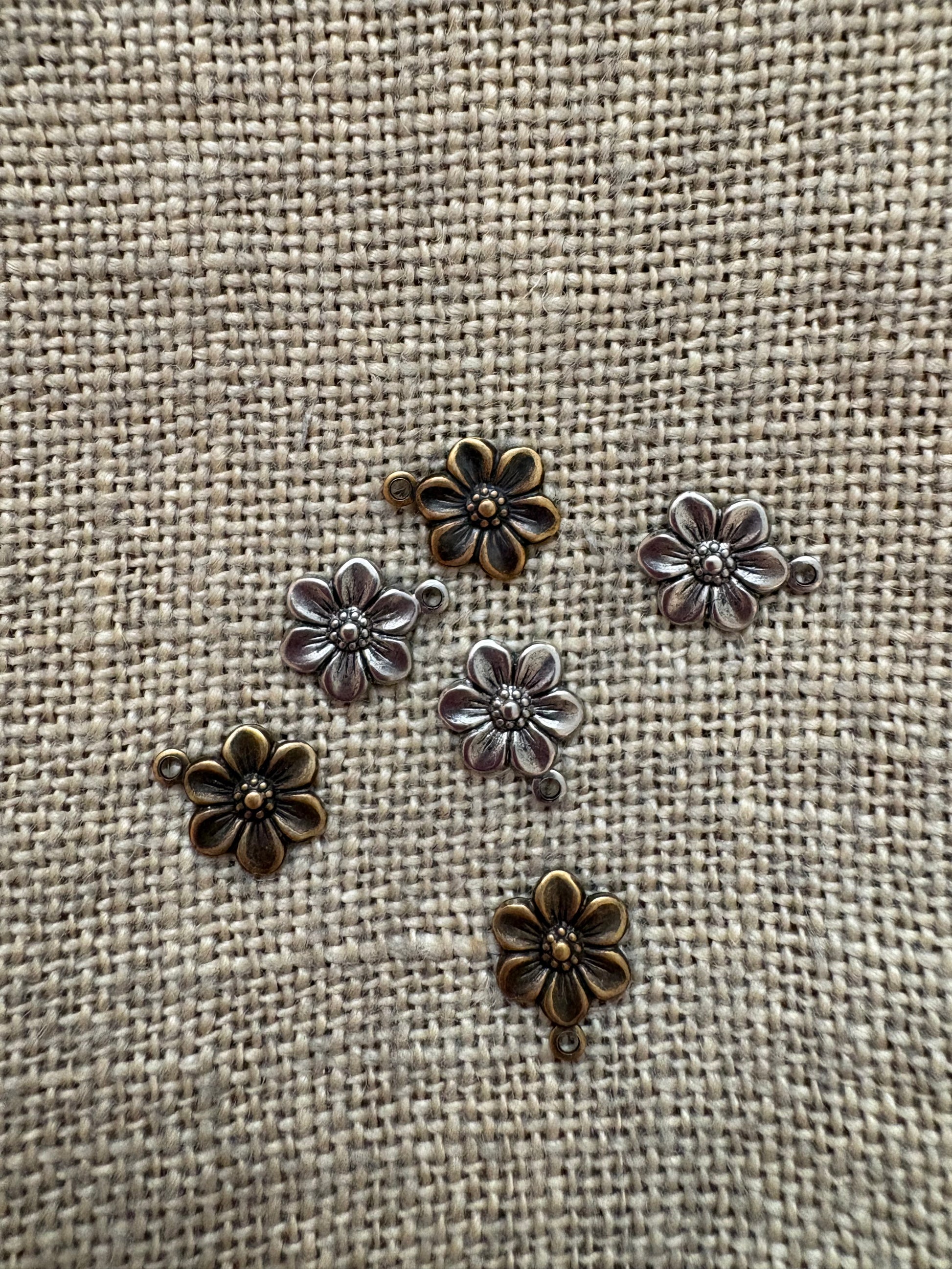 Bronze flower-shaped metal charms on a textured beige fabric background