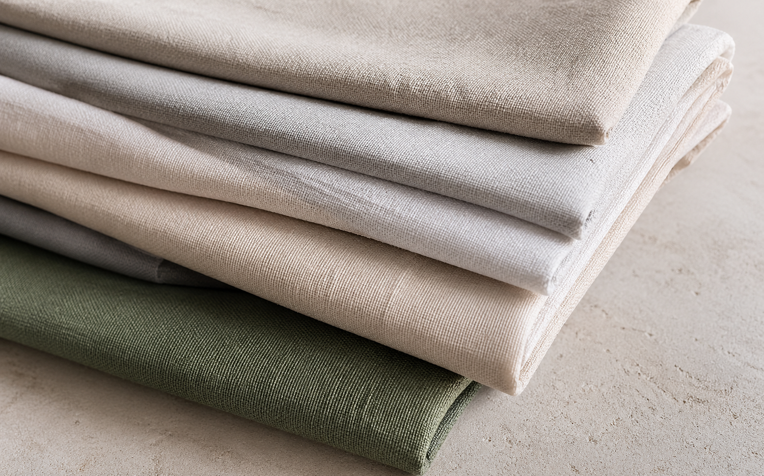 Stack of folded fabric sheets in beige and green on a light surface