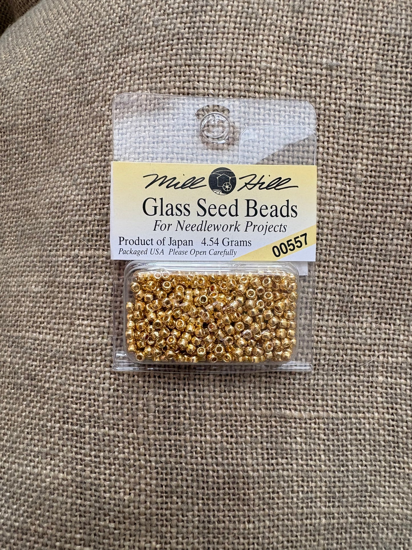 Packaged glass seed beads with a label on a textured fabric background