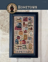 Framed cross-stitch pattern titled 'Hometown' on a textured fabric background.