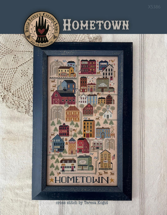 Framed cross-stitch pattern titled 'Hometown' on a textured fabric background.