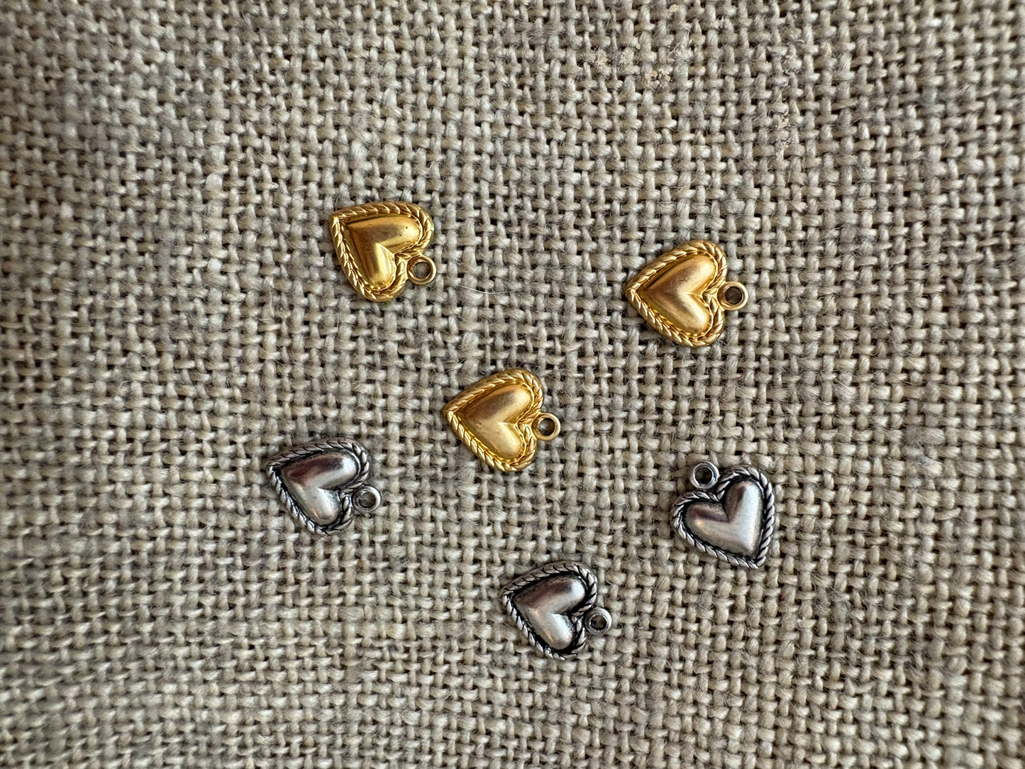 Heart-shaped metal charms in gold and silver on a textured fabric background