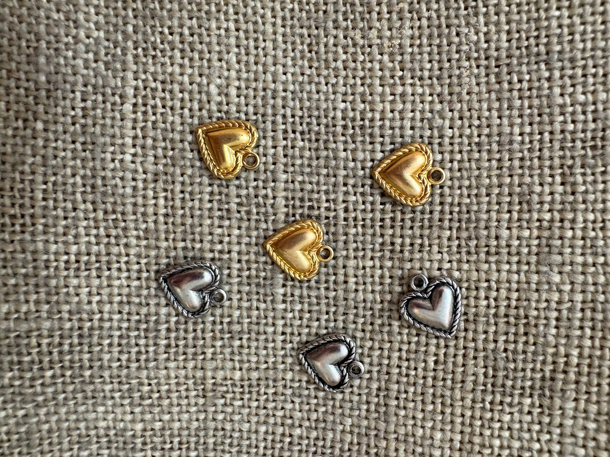 Heart-shaped metal charms in gold and silver on a textured fabric background