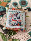Cross-stitched fabric piece on a quilt with scissors and buttons