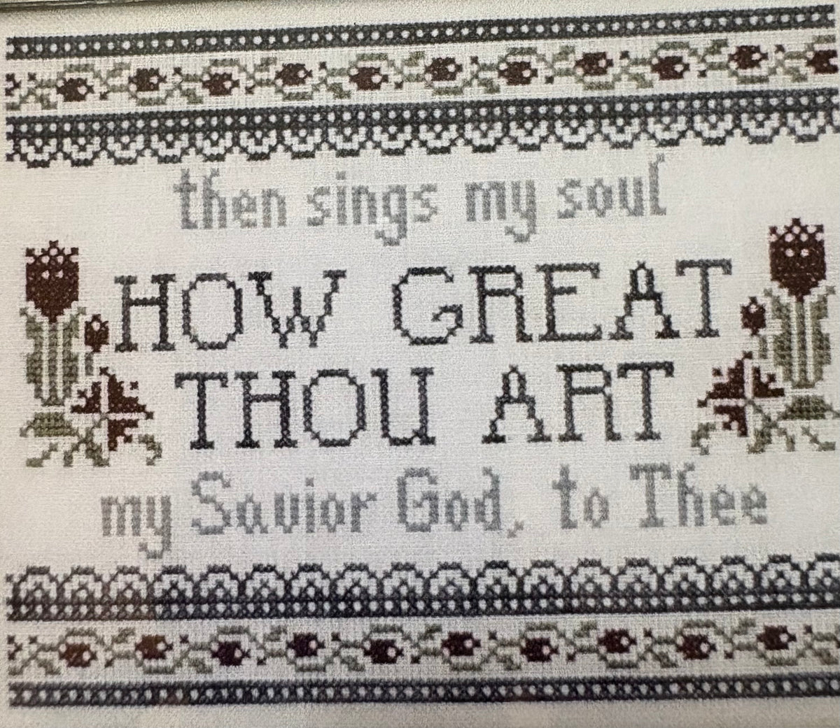 Cross-stitch embroidery featuring the Christian hymn 'How Great Thou Art' with decorative borders and floral motifs on a white fabric background.