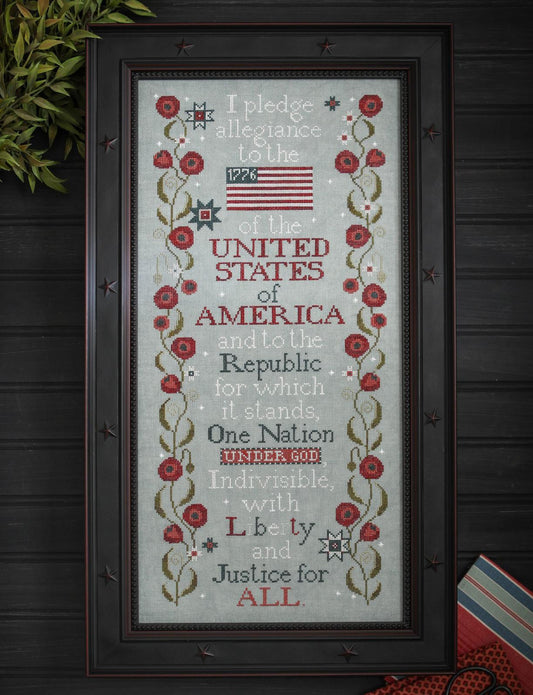 Framed cross-stitched piece with the Pledge of Allegiance and American flag on a wooden background.