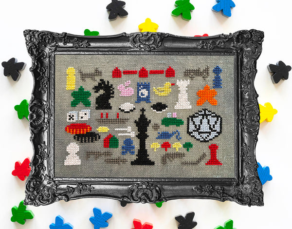 Framed cross-stitched art of chess pieces on a colorful background