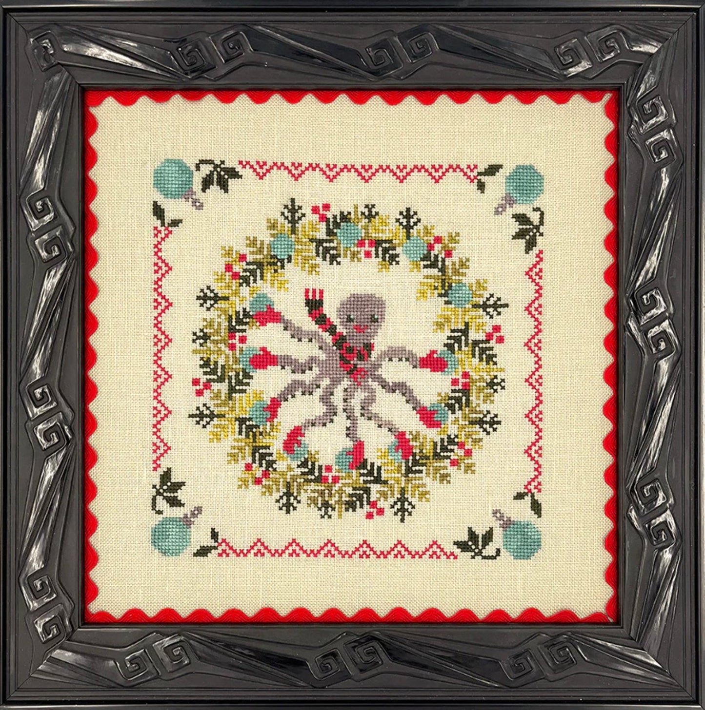 Decorative cross-stitched design with a skull and floral wreath in a decorative frame.