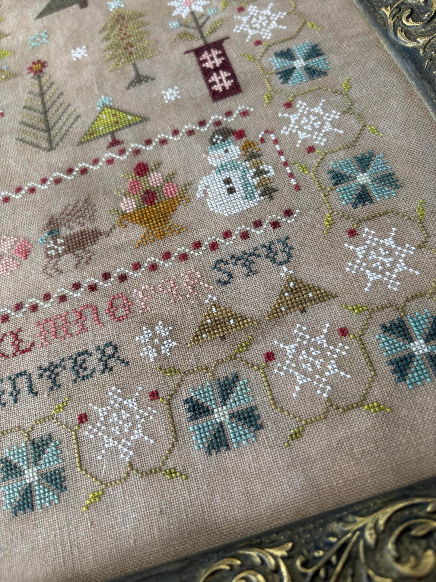 Close-up of a cross-stitched piece with winter-themed designs on beige fabric.