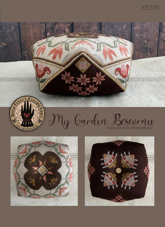 Embroidered fabric piece with geometric pattern on a wooden surface, featuring the brand 'My Garden Biscornu'.
