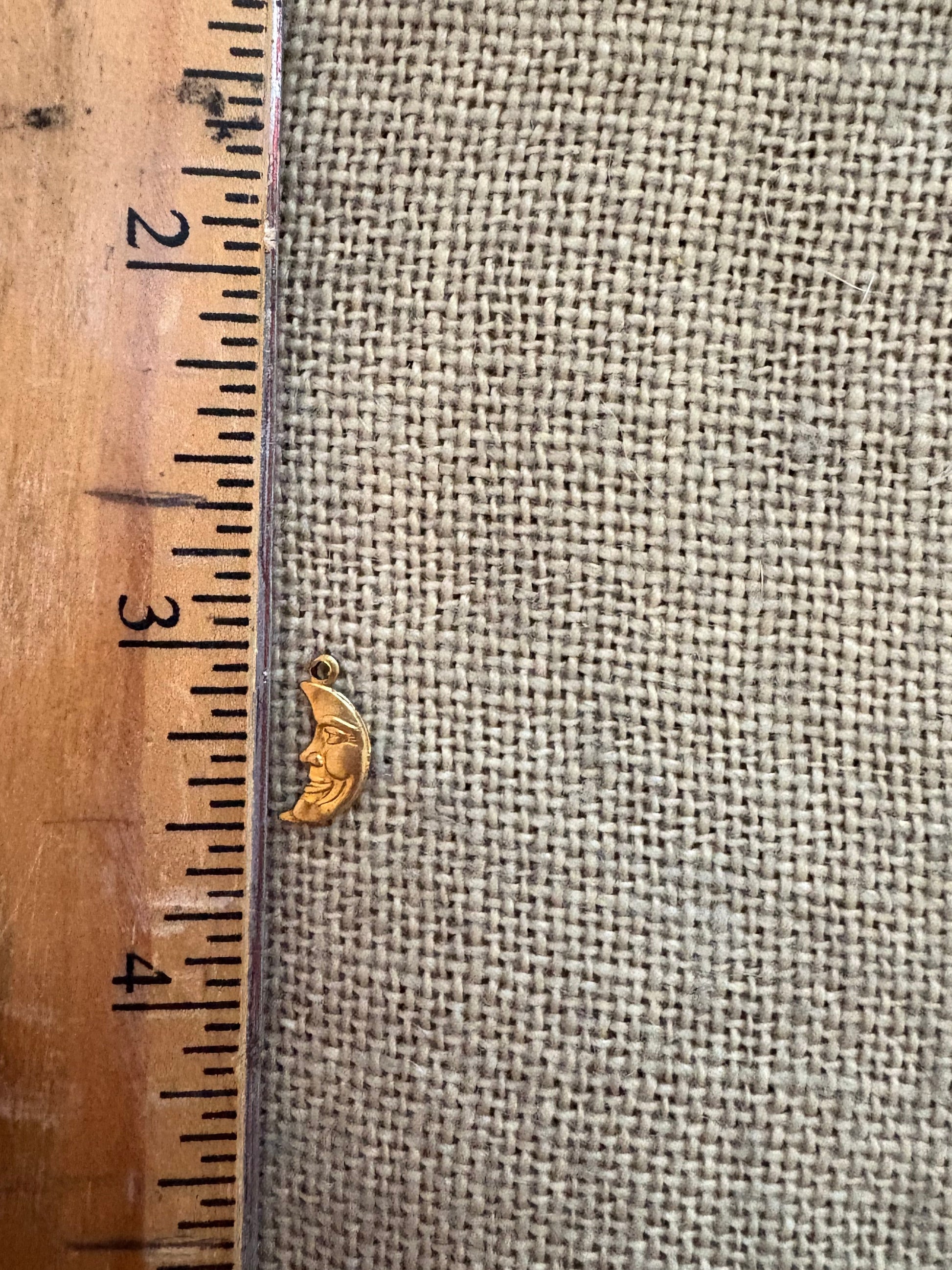 Small gold moon charm next to a wooden ruler for scale.