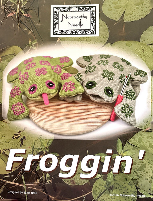 Cross Stitched frog  with a needle on a wooden board, surrounded by green leaves, with 'Noteworthy Needle' branding.
