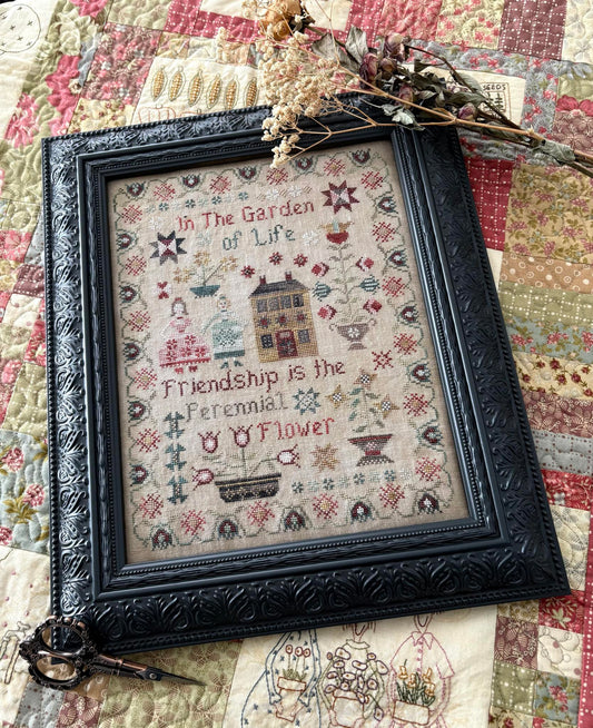 Framed cross-stitched sampler with decorative elements on a quilted background