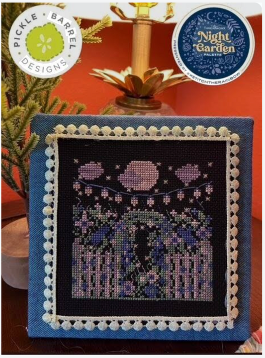 Cross-stitched piece with a night scene design on a blue fabric background, featuring Pickle Barrel Designs branding.