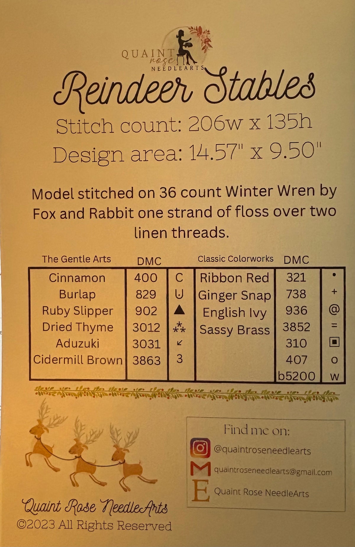 A beige fabric care label and pattern information card for 'Reindeer Stables' by Quaint Rose Needle Arts. The card features black text detailing stitch count, design area, and a color reference table, alongside illustrations of a Santa Claus figure and reindeer.
