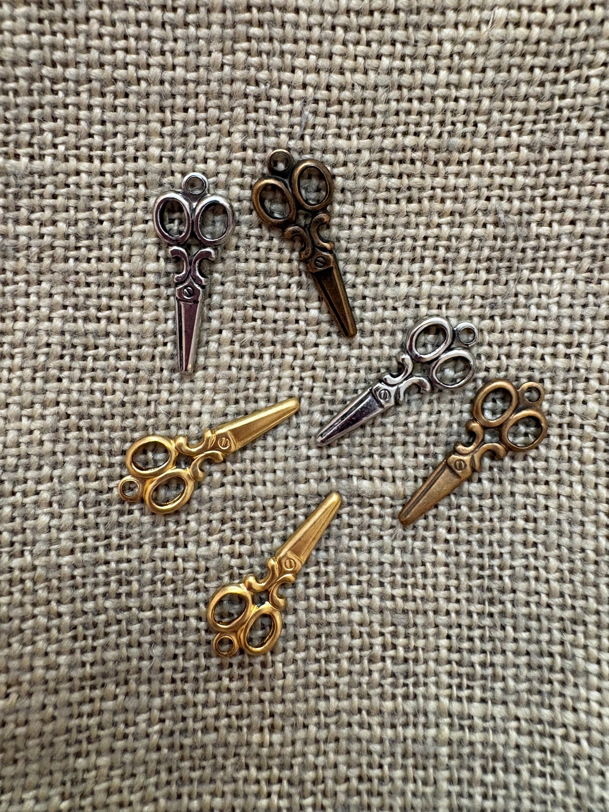 Collection of small scissors-shaped charms on a textured fabric background