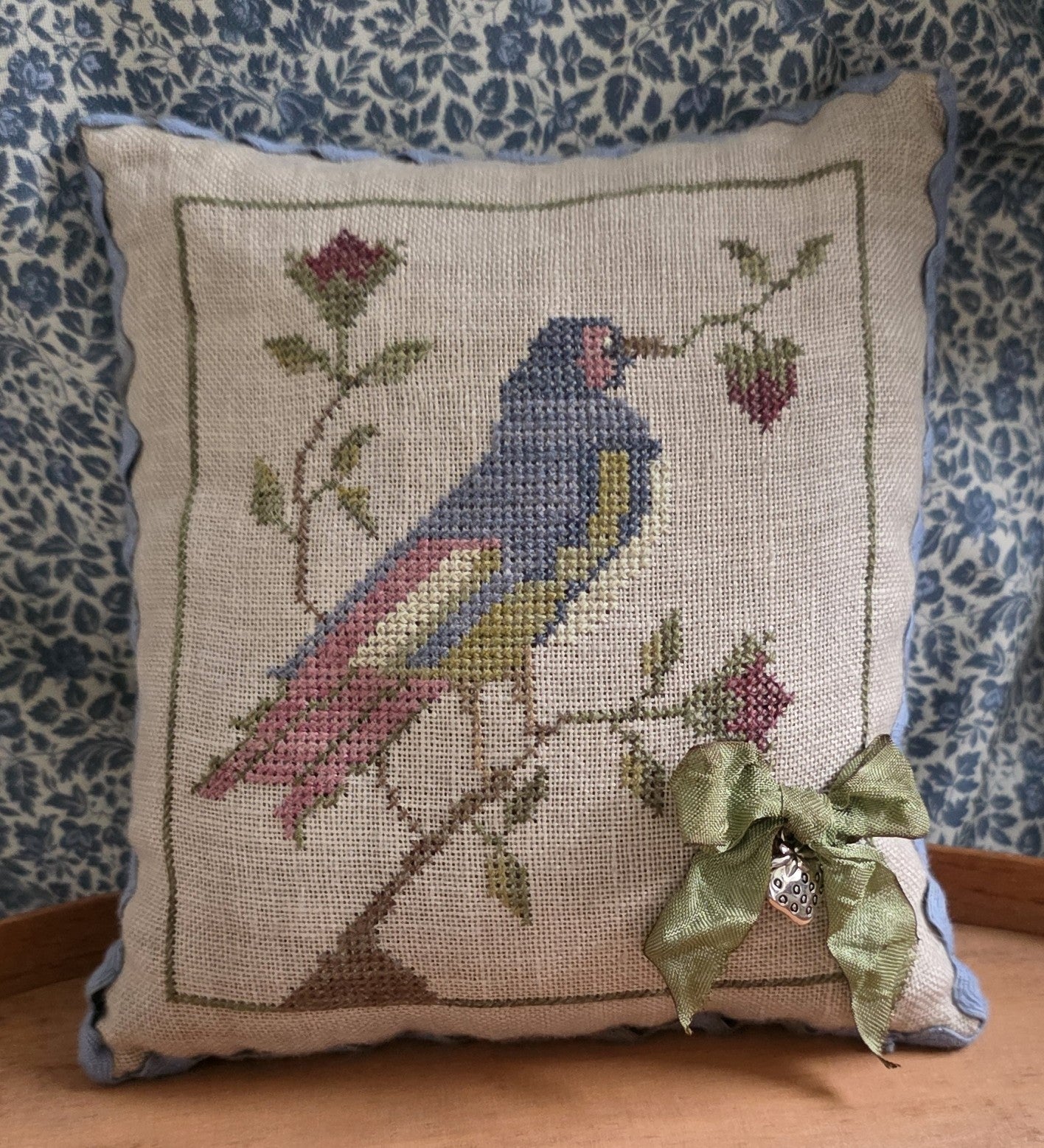 Decorative pillow with a bird and floral design on a blue patterned fabric background
