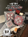 Patriotic Piecemakers cross-stitch pattern with decorative pillows and thread spools on a table.