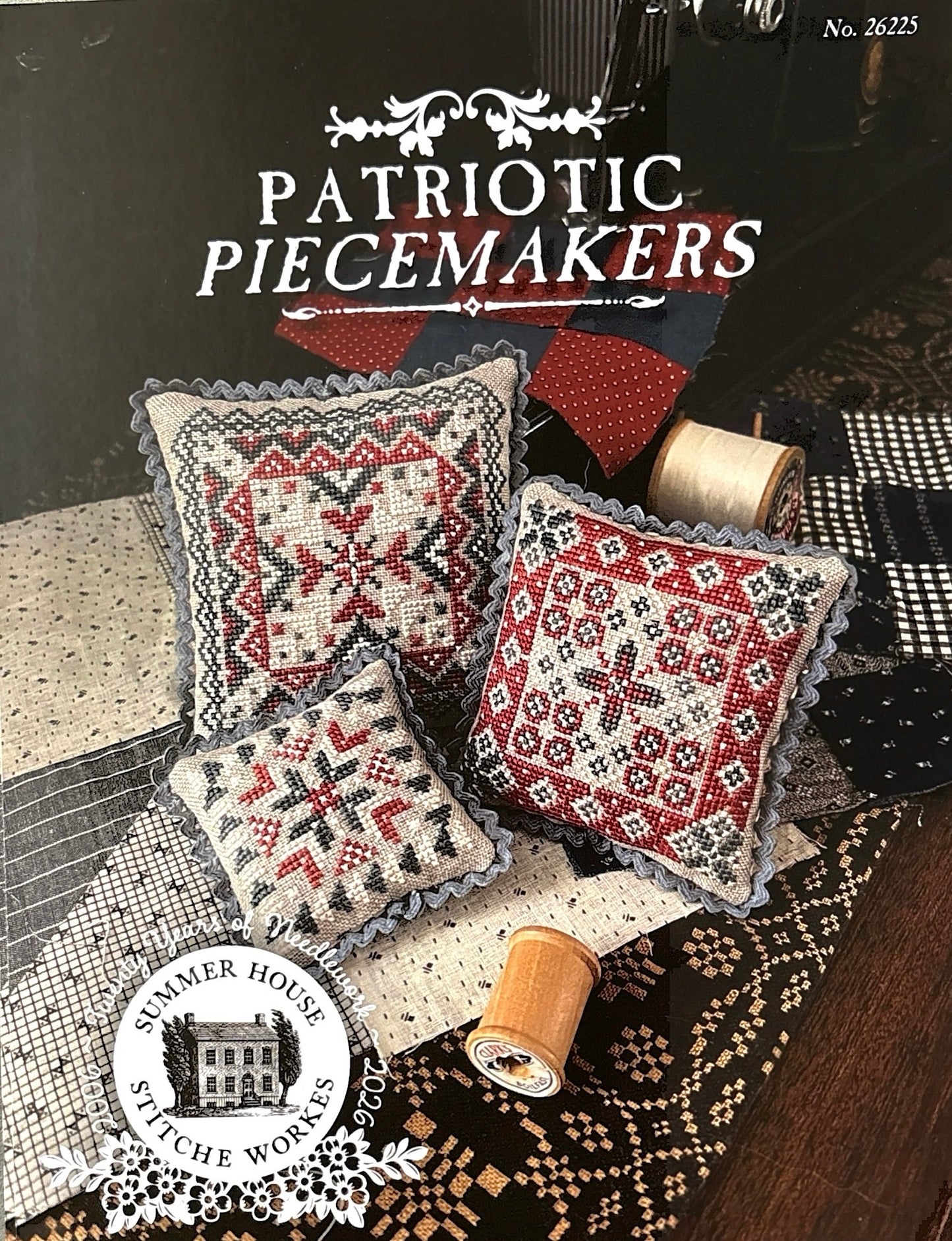 Patriotic Piecemakers cross-stitch pattern with decorative pillows and thread spools on a table.