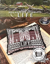 Cross-stitched pillow with 'LIFE' design on an open book, surrounded by rustic elements.