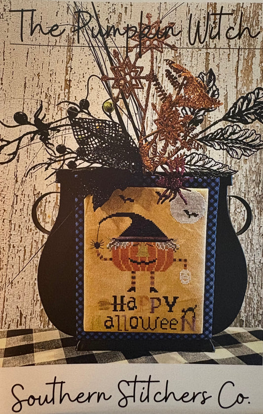 A Southern Stitchers Co. 'The Pumpkin Witch' cross-stitch pattern, featuring a black cauldron with a stitched pumpkin witch character and 'Happy Halloween' text, displayed against a rustic wood background.