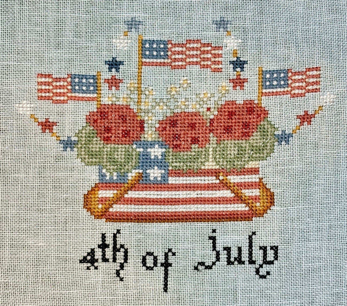 Cross-stitched design of a boat with July 4th decorations on fabric.