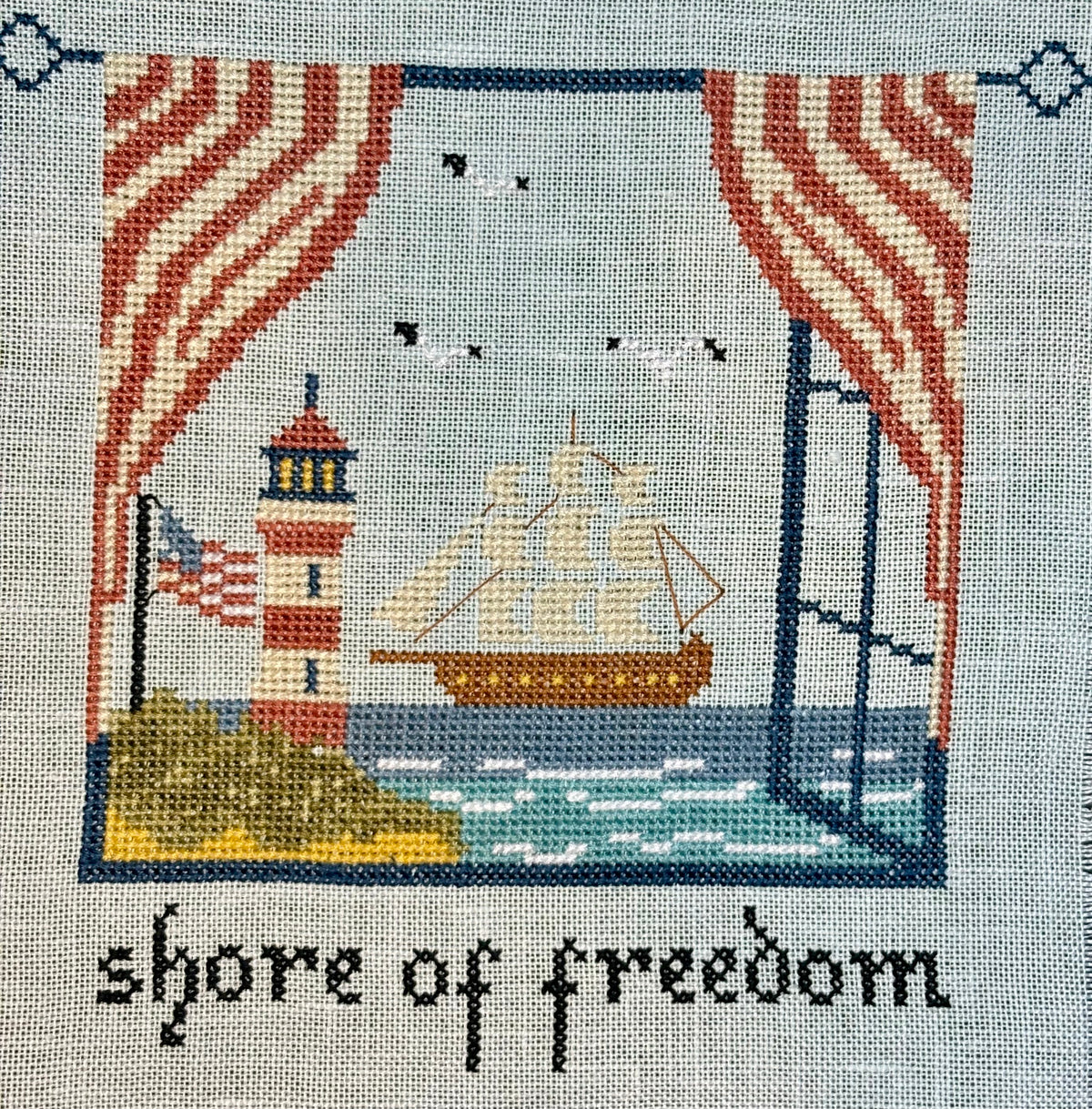 Embroidered design of a lighthouse, ship, and American flag with 'shore of freedom' text on a textured fabric background.