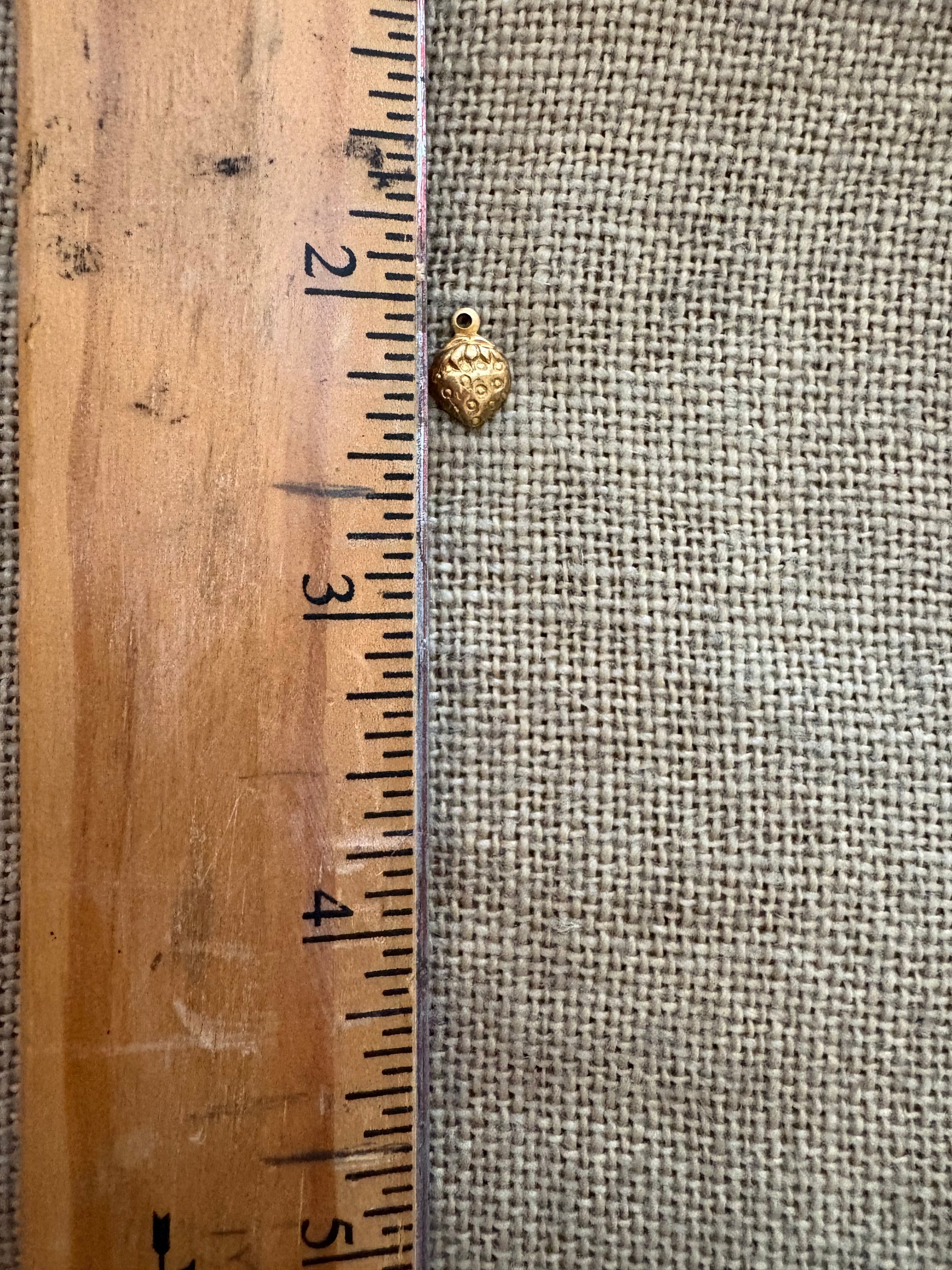 Small strawberry charmn next toa wooden ruler against a textured fabric background